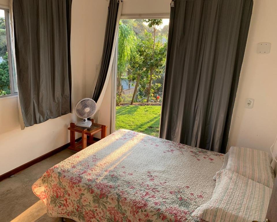 Quarto no Recanto Do Sossego com uma cama de casal com uma varanda ampla que dá direto para o jardim da propriedade