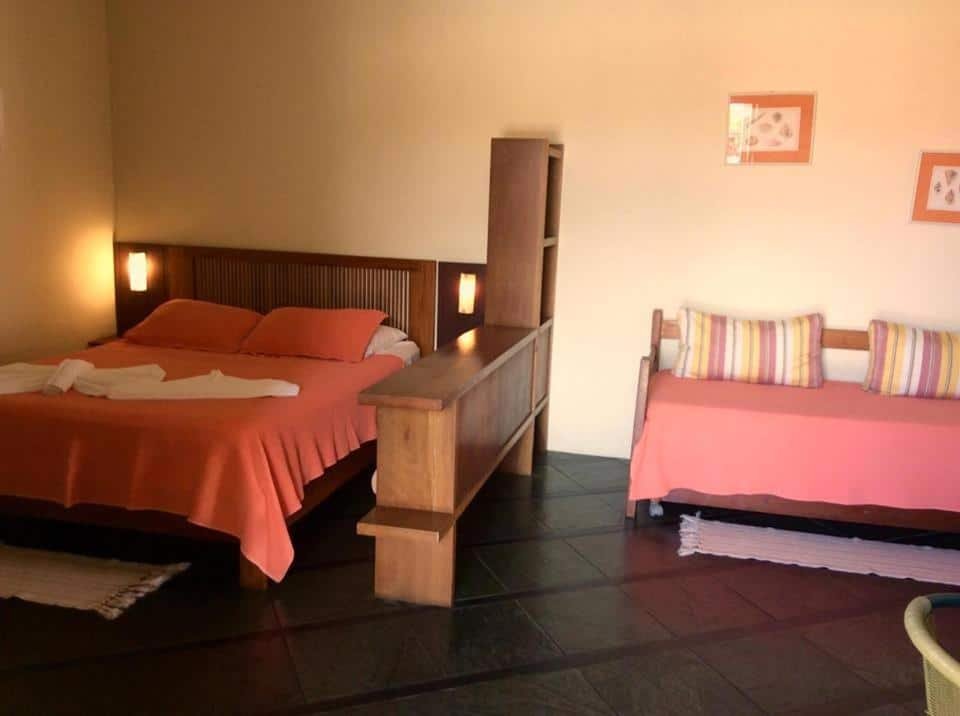 Quarto da Pousada Refugio Port Sahy com cama de casal no lado esquerdo, uma cômoda de madeira no meio e no lado direito sofá cama.
