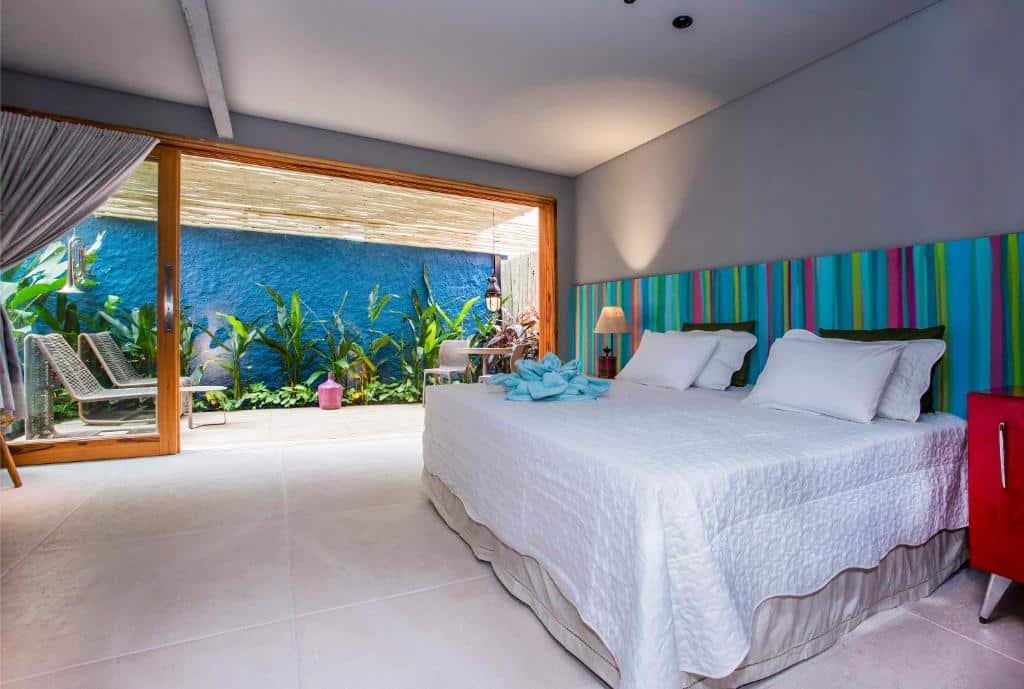 Quarto da Pousada Refúgio de Maresias com cama de casal ao centro do quarto e ao fundo área de estar com cadeiras.