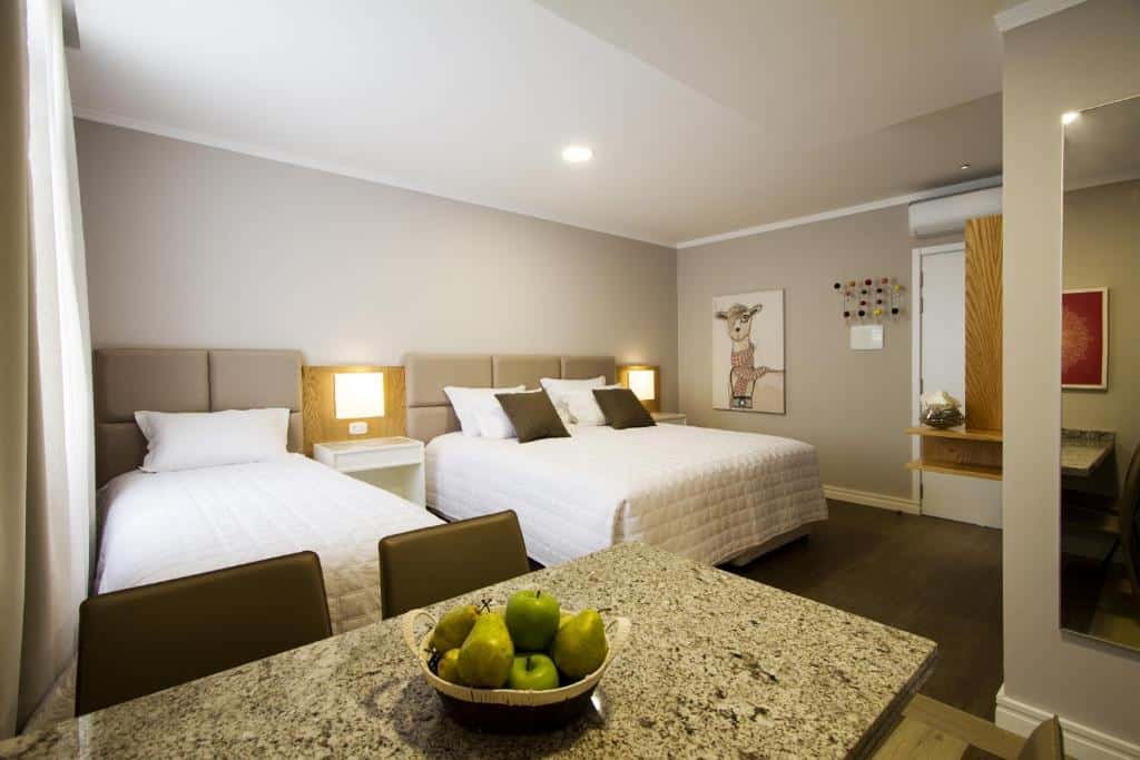 Uma cama de casal e uma de solteiro no Rosa Flat Charm Gramado, um espelho, uma televisão, dois abajures, um quadro e um ar-condicionado, para representar airbnb em Gramado