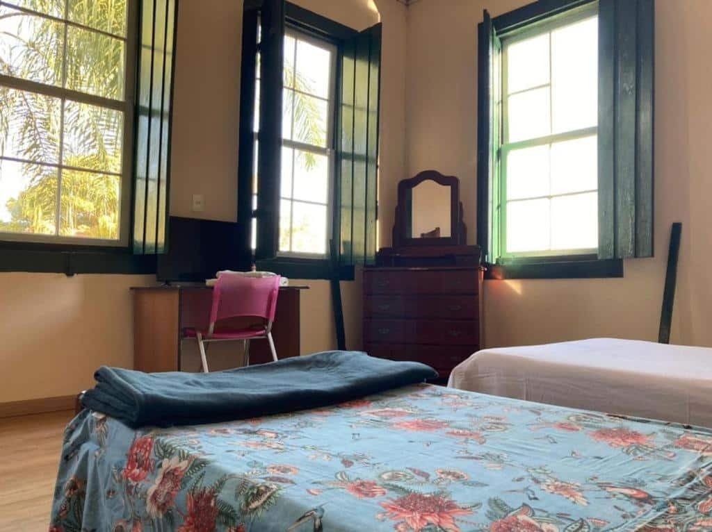 Quarto da Pousada Fazenda São Pedro com cama, TV e janelas de madeira.