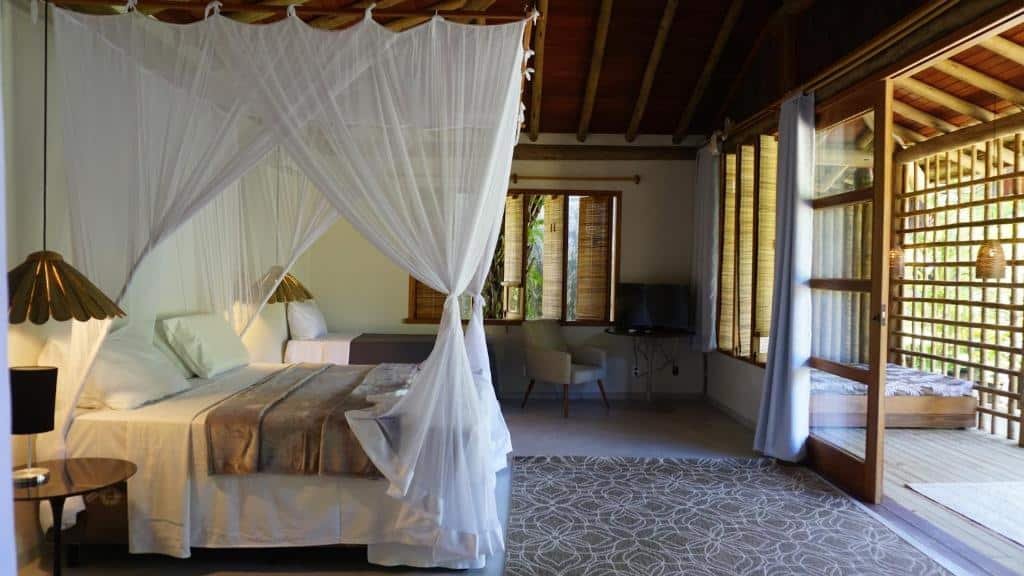 Quarto do Soleluna Casa Pousada com uma cama de casal do lado direito e do lado esquerdo cama de solteiro com TV e poltrona a frente da cama de solteiro e em frente a cama de casal portas de madeiras que dá acesso a varanda.