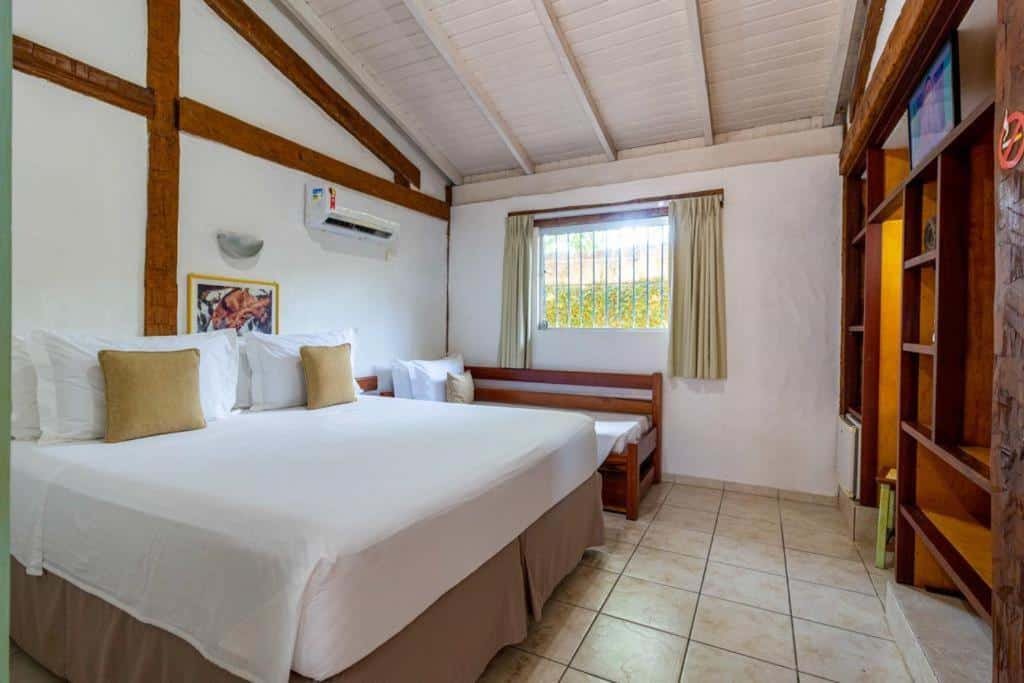 Quarto da Pousada Tambayba com cama de casal no centro do quarto, do lado esquerdo sofá cama e janela com cortinas bege.
