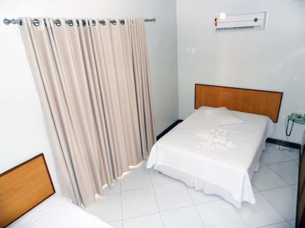 Quarto no Itaparica Praia Hotel com uma cama de casal e uma de solteiro, uma sacada com cortinas, para representar pousadas em Vila Velha