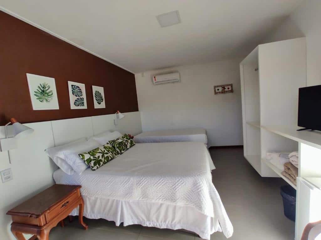 Quarto do Terrazzo Suites, uma cama de casal, uma de solteiro, um armário, um ar-condicionado, uma televisão, dois abajures, três quadrinhos na parede e algumas toalhas e almofadas, para representar pousadas em Escarpas do Lago