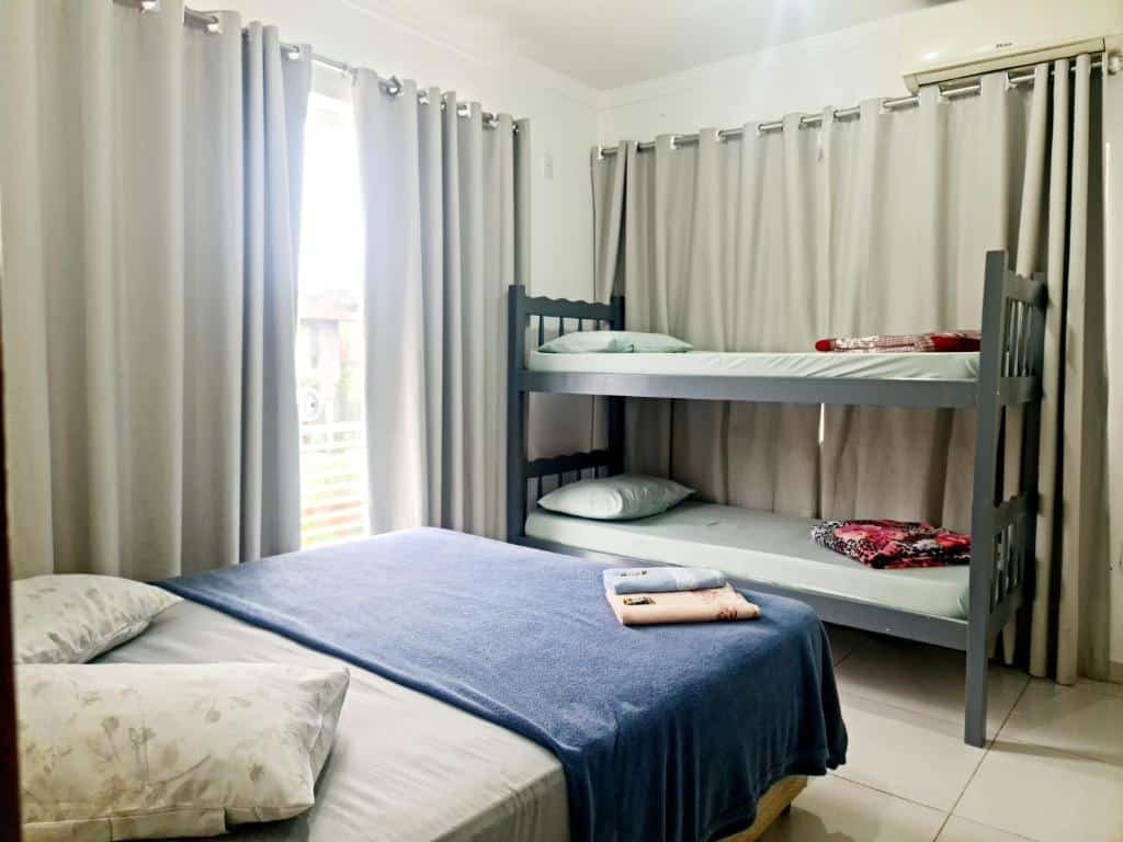 quarto da Valentina Ramos Pousada com uma cama de casal no canto inferior esquerdo, e com uma beliche em frente aos pés da cama de casal. É possível ver uma porta de vidro no lado esquerdo com acesso à uma varanda particular.
