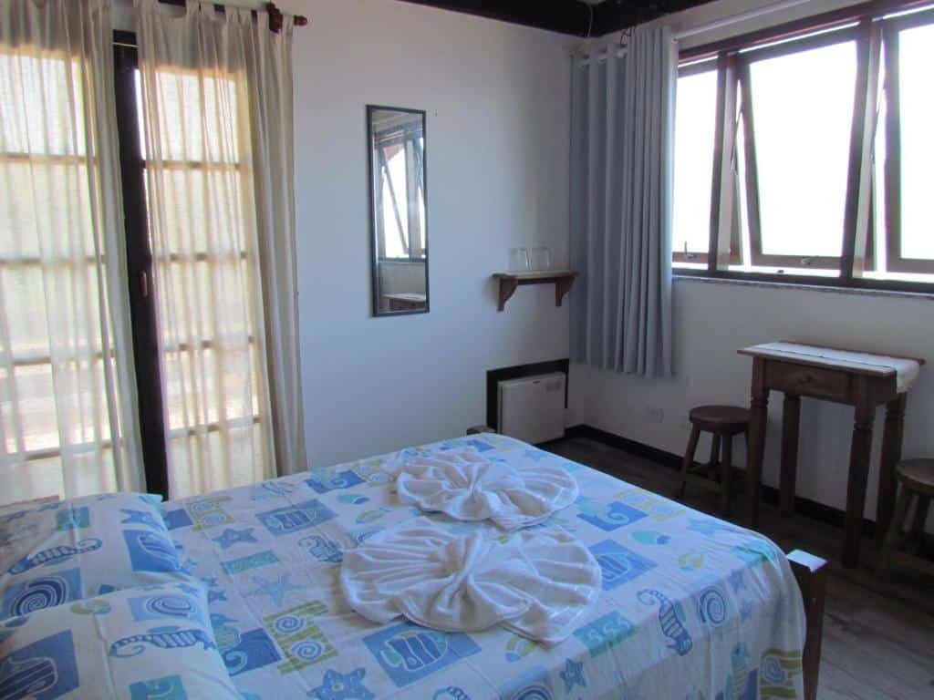 Quarto da Pousada Victoria Reggia com cama de casal, uma cômoda de madeira em frente a cama com duas cadeiras de madeira.