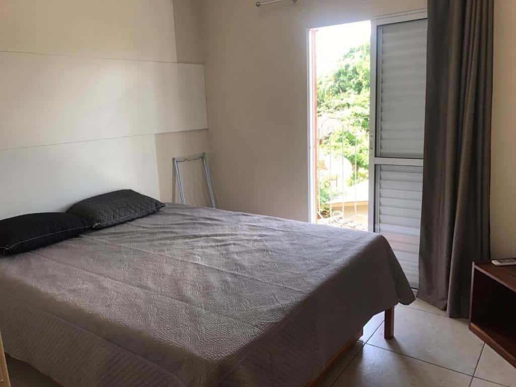 Quarto em Villa Bela Flats Ubatuba, uma cama de casal, uma sacada e uma televisão, para representar pousadas na Praia da Enseada em Ubatuba