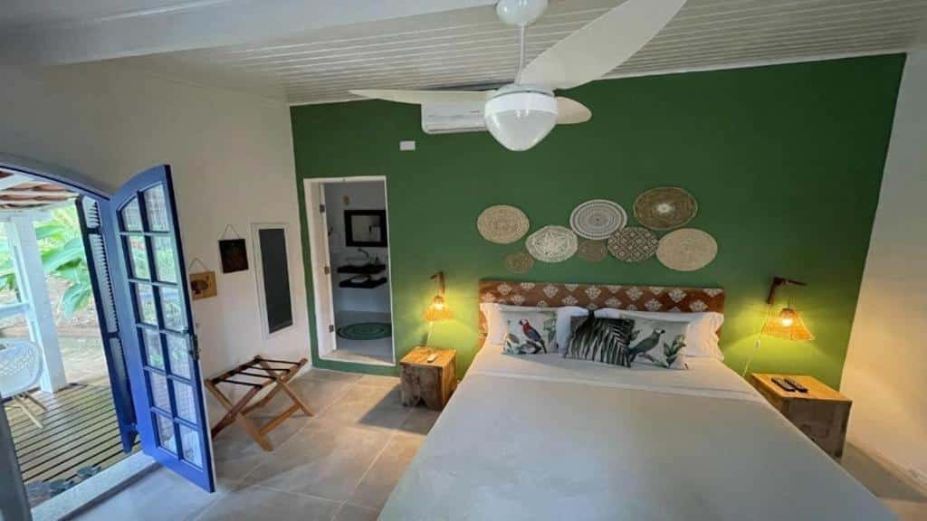 Quarto do Village Toque Toque com cama de casal, duas cômodas ao lado da cama com luminárias, do lado esquerdo portas de madeiras azul com acesso a varanda.