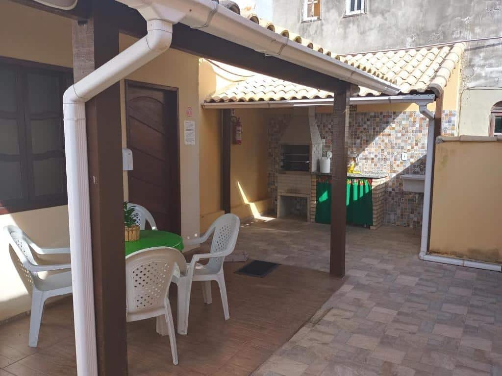 Quintal do airbnb Casa da Celia. No canto direito há uma área coberta com churrasqueira, pia e um tanque de lavar roupa. Já no lado esquerdo há outra parte coberta com uma mesa redonda e quatro cadeiras em volta. Ainda no lado esquerdo há uma porta que dá acesso a área interna da casa.