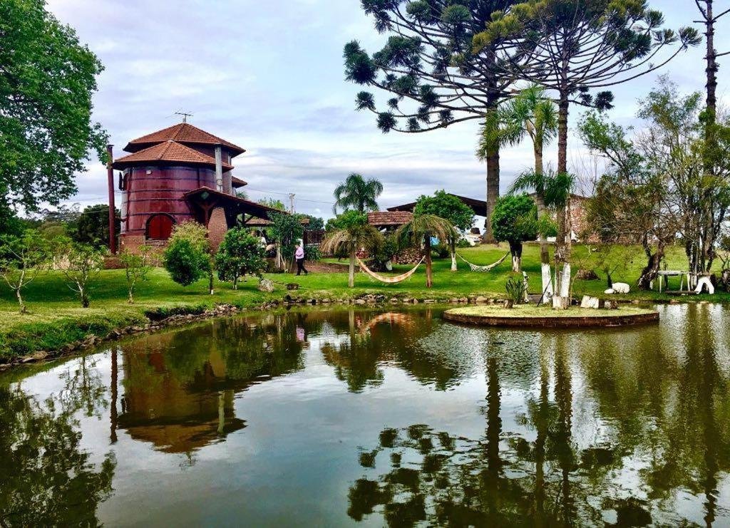 Lago no interior do Recanto das Pipas, uma das pousadas em Bento Gonçalves, com construções em forma de pipa ao fundo e árvores com rede