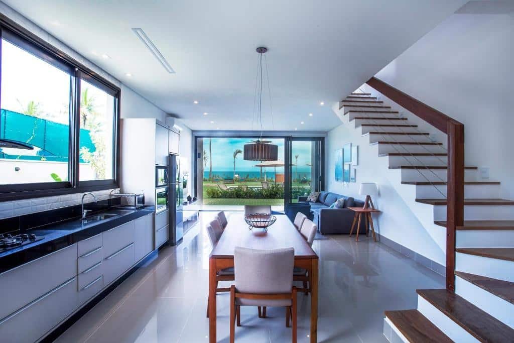 Cozinha e sala no Residencial Marina Del Sol. A cozinha é espaçosa, há uma mesa de jantar no centro, uma escada na direita e pia à esquerda. A sala está no fundo.