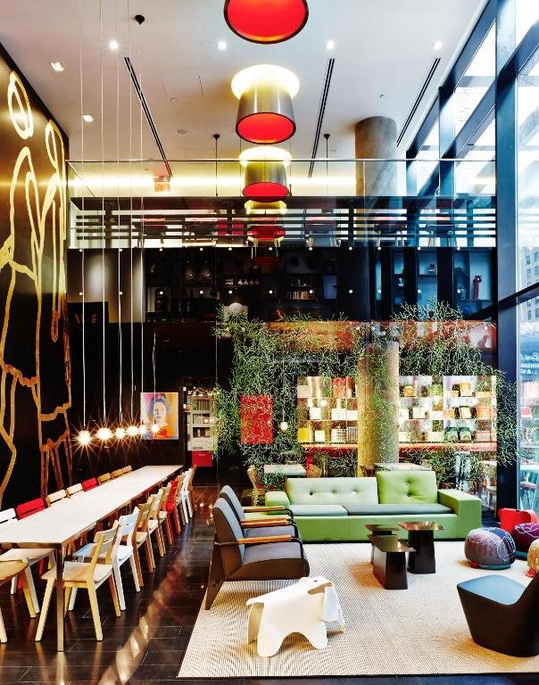 refeitório do citizenM New York Times Square com uma ampla mesa de jantar à esquerda e uma área de lounge compartilhado à direita, com sofás e pufes.