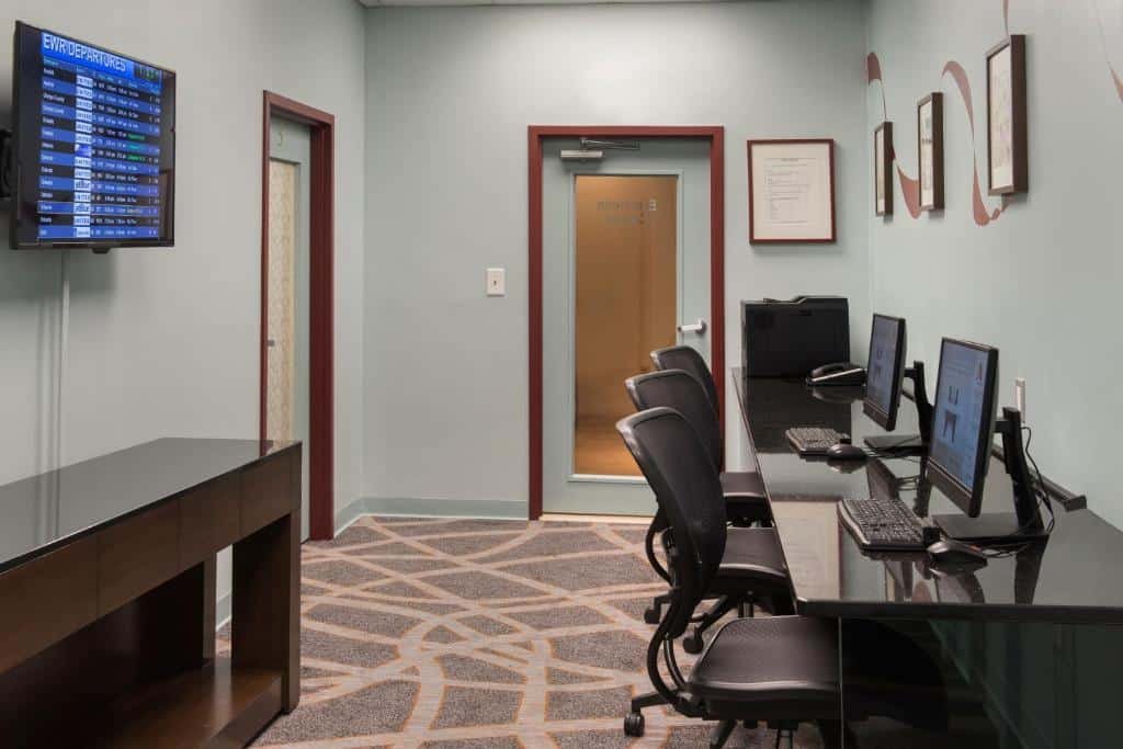 Imagem de uma sala de reuniões bem iluminada e elegante, localizada no Newark Liberty International Airport Marriott. A sala possui uma decoração contemporânea com cadeiras confortáveis dispostas em torno de uma grande mesa retangular. As paredes são revestidas com um papel de parede sutil em tons neutros, e quadros artísticos adornam as superfícies. A iluminação é suave, vinda de luminárias embutidas no teto, criando uma atmosfera profissional e acolhedora. A sala de reuniões está localizada em um dos hotéis perto do aeroporto de Newark, oferecendo comodidade para viajantes e profissionais em trânsito