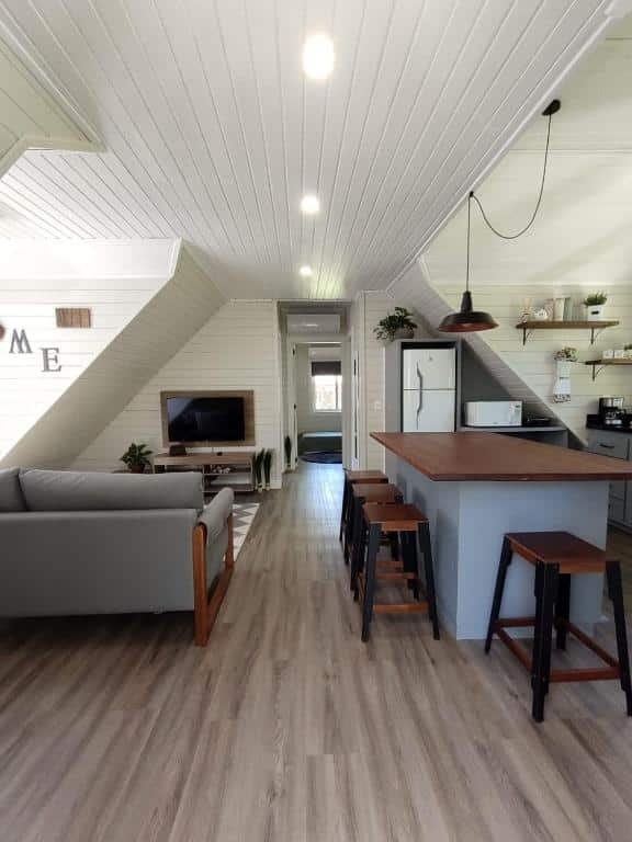 Sala de estar do Family House Gramado, um balcão com quatro lugares para sentar, um sofá, uma televisão e uma pequena cozinha