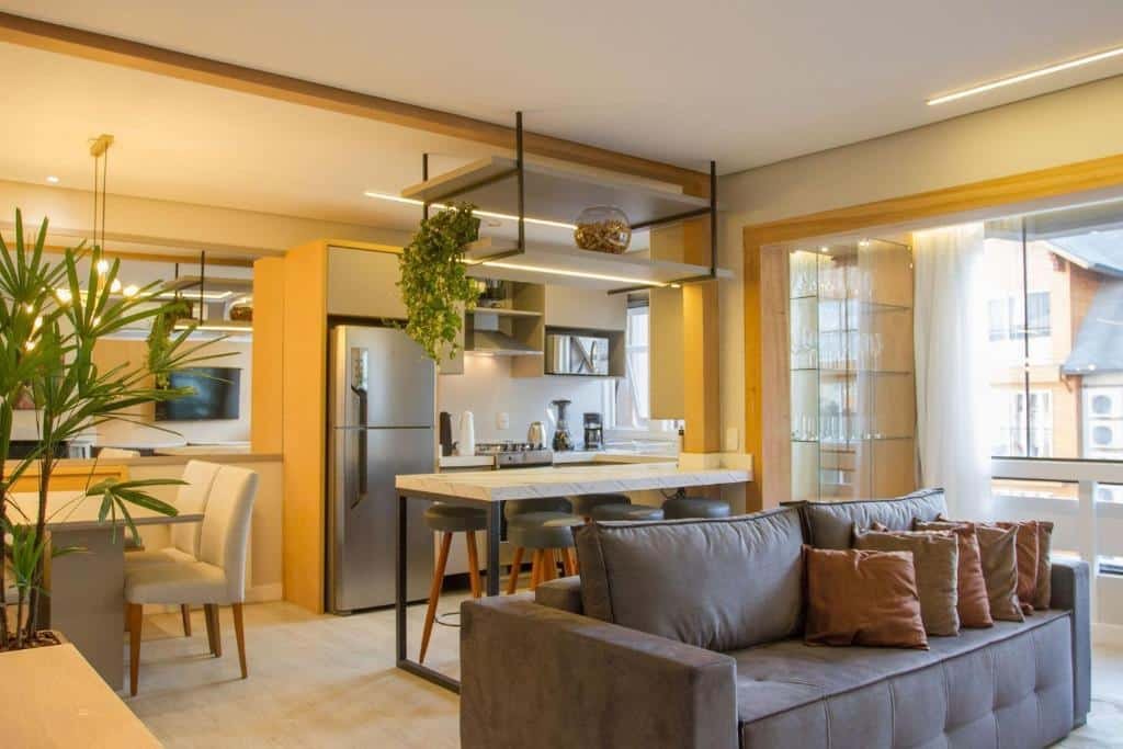 Sala de estar do Incrível apartamento no Centro de Gramado , decoração minimalista, algunas plantas, um balcão com seis lugares, uma mesa com quatro lugares, uma sofá com almofadas e uma sacada envidraçada