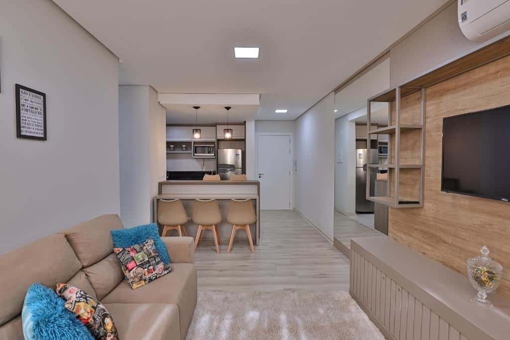 Sala do RESIDENCIAL LONDON ALPHAVILLE AP 104, local amplo, um balcão com seis lugares, um sofá com almofadas, uma televisão, um espelho e uma pequena cozinha compacta