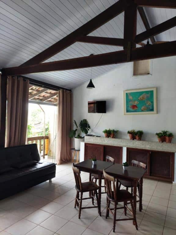 Sala de estar do Solaris do Unacom duas mesas pequenas com quatro cadeiras de madeira a frente do lado esquerdo um sofá de couro.