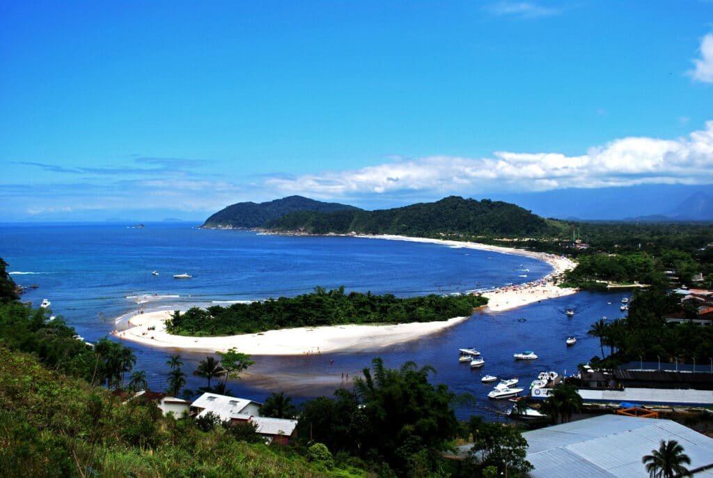 Vista de cima da Barra do Una, São Sebastião durante o dia com mar azul e barcos no mar.