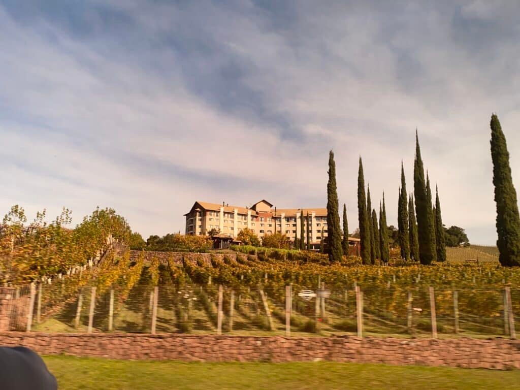 Estrutura externa do Spa do Vinho, um dos hotéis em Bento Gonçalves, visto da estrada que passa em frente, sendo que há vinhas e árvores em frente ao prédio da hospedagem