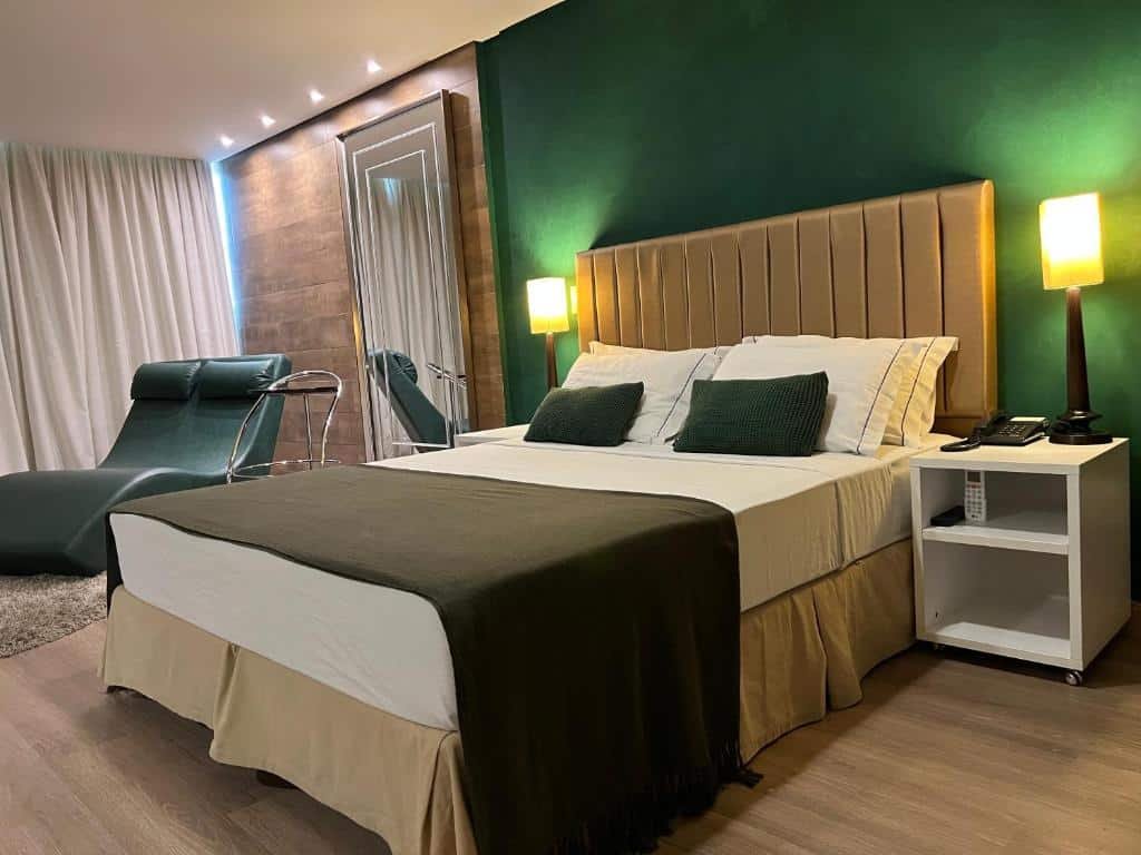 Suíte do Alfa Hotel. A cama está no lado direito do quarto, há pequenas cômodas em cada lado da cama e no lado esquerdo há uma poltrona. Imagem para ilustrar o post hotéis em Viçosa.