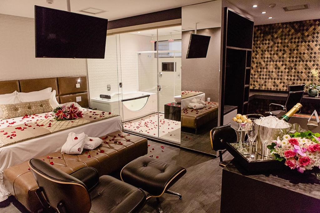 Quarto do Bristol Viçosa Hotel. A cama está no lado esquerdo do quarto, no lado direito está o banheiro com uma banheira de hidromassagem e na frente há uma poltrona, TV, mesa com cadeira e armário. Imagem para ilustrar o post hotéis em Viçosa.