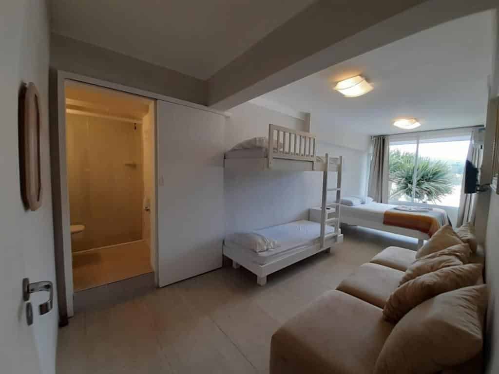 Suíte da MANSÃO TENÓRIO - Suítes, Estudio ou Cobertura Pé na Areia, um sofá, uma beliche e uma cama de casal, além de um banheiro e uma janela com vista para praia