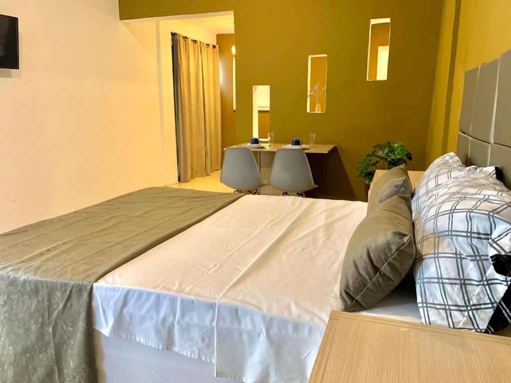 Quarto do Temporada Litorânea slz com uma cama de casal com travesseiros e almofadas, mais ao lado há uma pequena mesa com duas cadeiras e uma televisão