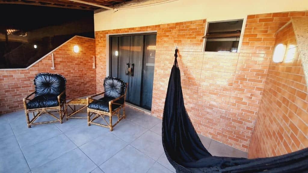 Varanda do airbnb Arraial do Cabo - Praia do Pontal. No lado direito há uma rede de descanso, no lado esquerdo há duas poltronas com uma mesinha no meio e atrás há uma porta de vidro que dá acesso ao airbnb.