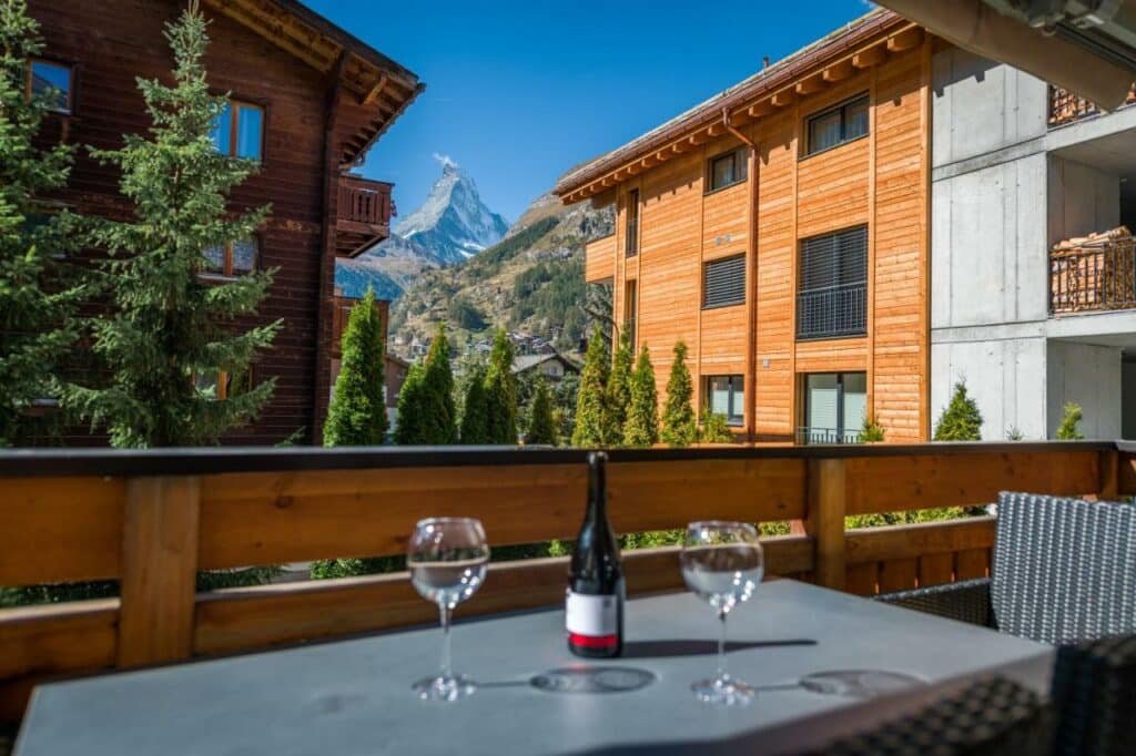 Varanda da Casa Della Luce Apartments com uma mesa quadrada com duas taças e uma garrafa de vinho em cima da mesa do lado direito uma cadeira e a varanda tem vista para a estadia e árvores.