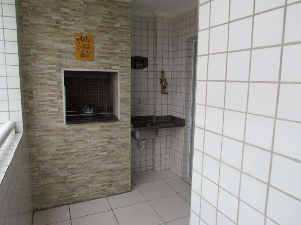 Varanda de apartamento com paredes de azulejo branco, pia no lado direito e churrasqueira no lado esquerdo.