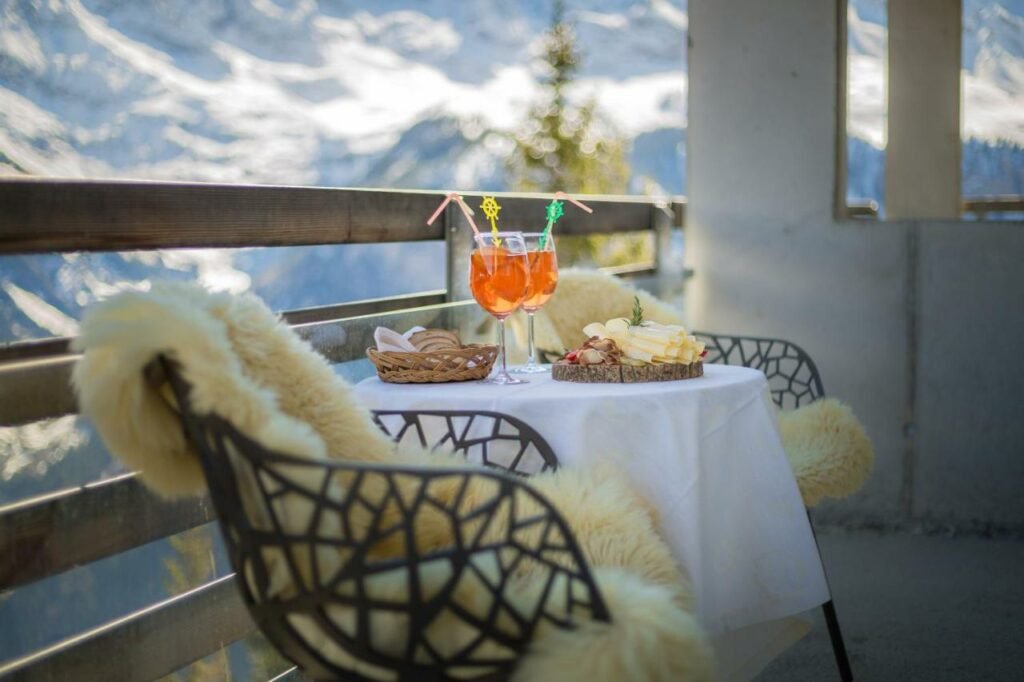 Imagem de uma mesa na varanda do Hotel Edelweiss Superior com duas cadeiras em cima da mesa alguns frios, pães e duas taças com driks.