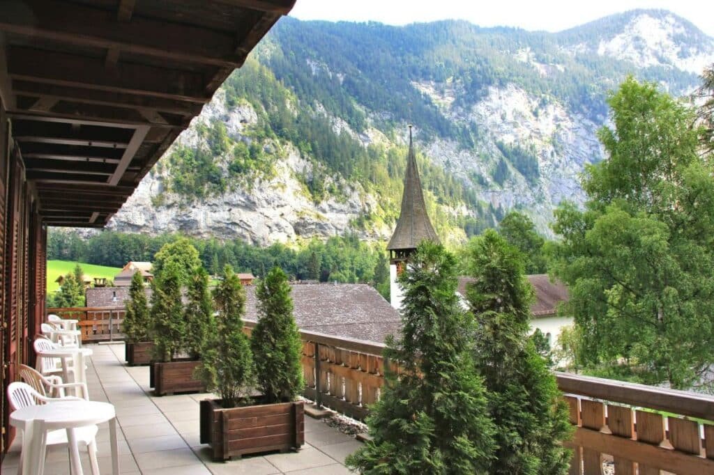 Imagem da varanda do Hotel Staubbach durante o dia com a varanda do lado esquerdo da imagem com cadeiras e mesas.