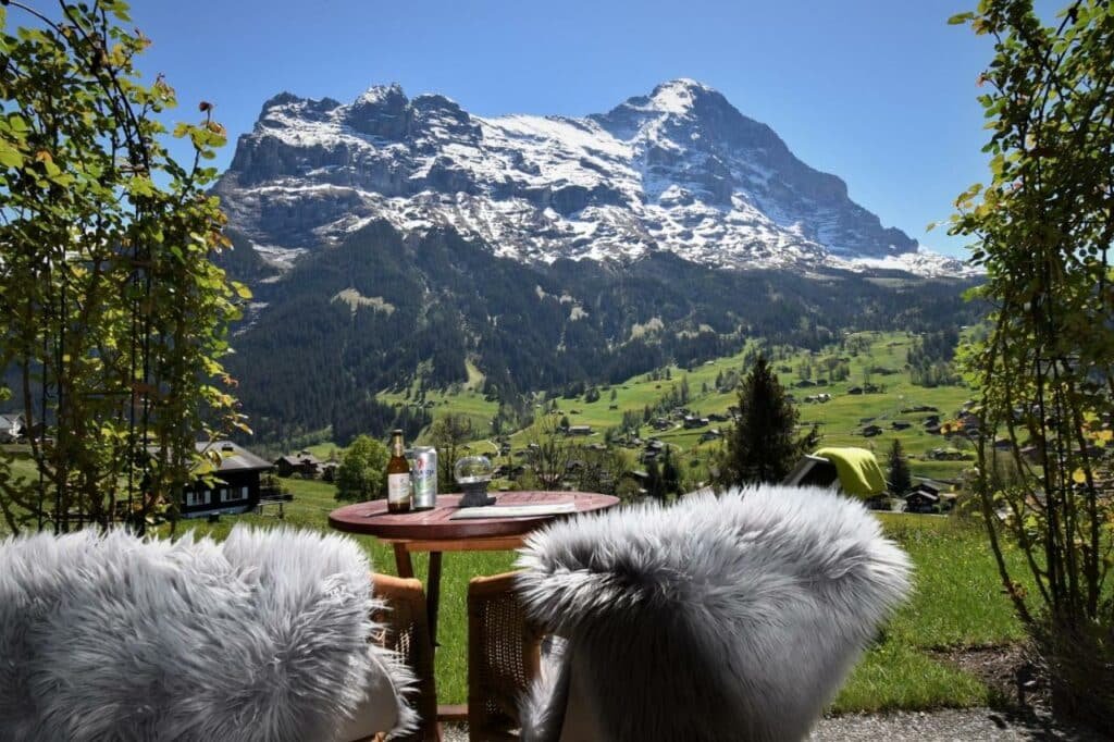 Imagem da varanda térrea do Hotel Cabana com duas cadeiras e uma mesa redonda com vista para as montanhas.