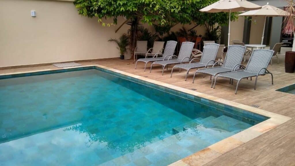 Piscina Villa Bela Flats Ubatuba, com cadeiras ao redor e algumas árvores e vasos de plantas