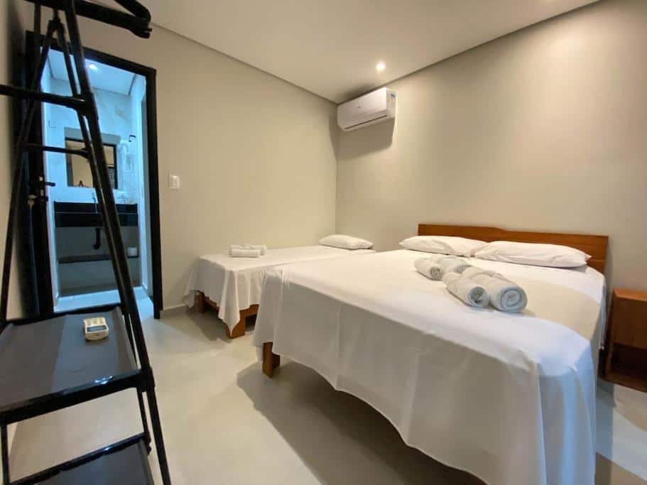 Quarto da Villa Licuri Boiçucanga. Uma cama de casal e uma de solteiro estão lado a lado. Perto delas está uma prateleira e a porta do banheiro.