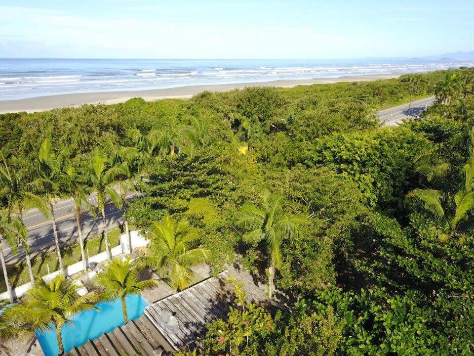 Vista do Camping Pousada Ilha do Mel - Frente ao Mar 
Reservar. Uma piscina e o telhado da pousada no lado esquerdo. Ao redor muitas árvores e na frente da pousada uma rua, mais árvores e a praia.