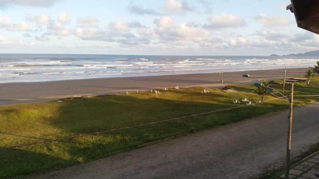 Vista do quarto da Pousada Peruíbe Ametista. Uma rua na frente, grama e o mar.