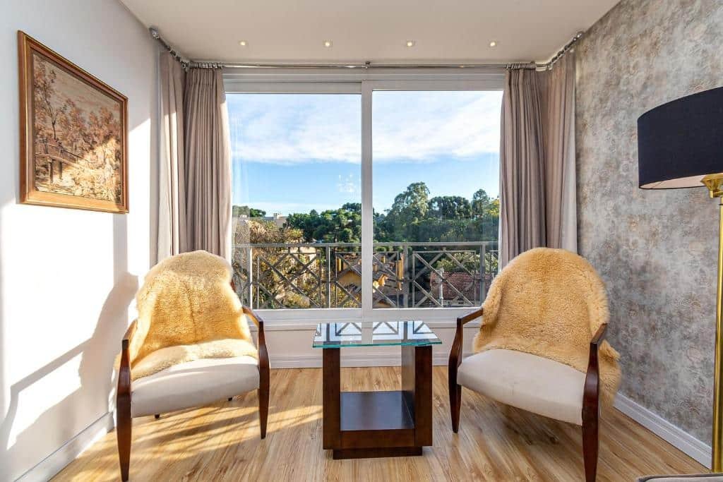 Sala do Rosa Apartamento Giovani Pizetta, duas cadeiras com toalhas de pelinhos com uma bela vista logo atrás por um janela ampla e envidraçada