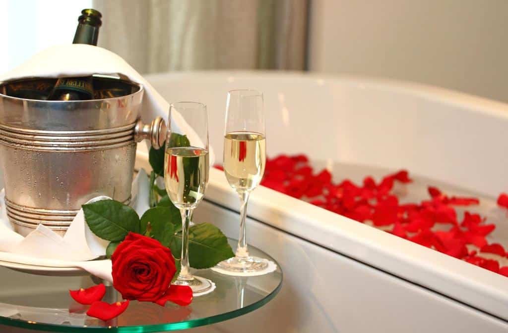 Foto de perto da hidro disponível no Waldstätterhof Swiss Quality Hotel. Há pétalas de rosa na água. Do lado da manheira há uma mesa com um balde de champagne e taças em cima.
