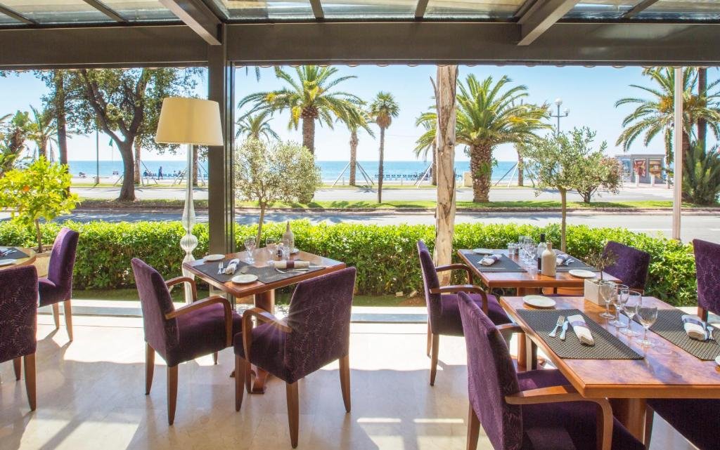 Uma das áreas de refeições do Westminster Hotel & Spa Nice. Há diversas mesas com cadeiras e um abajour de chão bem ao lado de uma avenida beira-mar.
